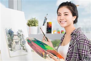 Young woman standing in front of an easel, holding a paint-covered palette.